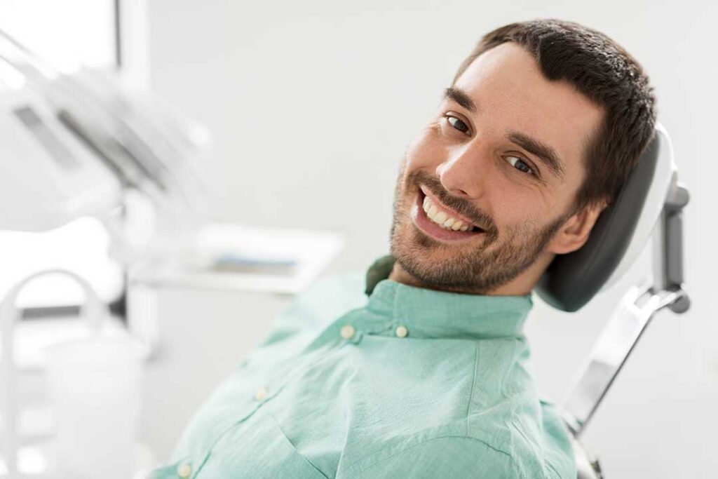 Person comparing an electric and manual toothbrush beside toothpaste and a bathroom sink.